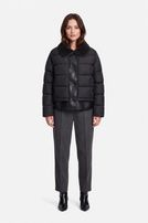 Frau trägt schwarzen Puffer-Jacken-Blazer mit Hosenanzug und schwarzen Stiefeln, elegant und schlicht.
