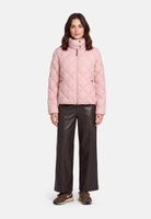 Frau trägt hellrosa Quilted-Jacket mit schwarzer Lederhose und braunen Sneakern.
