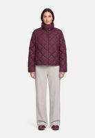 Frau trägt burgunderfarbenen Quilted-Jacket mit hellgrauen Hosen und flachen Schuhen.