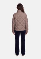 Frau trägt beige Quilted-Jacket mit hochgeschlagenem Kragen und dunkle, weite Hosen.