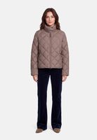 Frau trägt beige Quilted-Jacket mit Reißverschluss und dunkle, weite Hose.