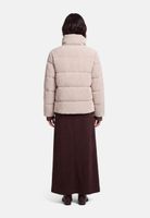 Frau trägt beige Daunenjacke mit Reißverschluss und langen maronenfarbenen Rock, Rückansicht.