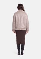 Frau trägt beige gefütterte Jacke mit dunklem, langem Wickelrock und Stiefeln.
