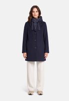 Frau trägt navy-blauen oversize-Mantel mit Kapuze und Bow, weiße Hosen, beige Schuhe.