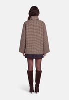 Frau trägt tweedartigen oversize Blazer, kurze dunkle Röcke und braune Stiefel, von hinten fotografiert.