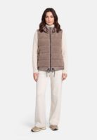 Frau trägt beige Daunenweste über cremefarbenem Rollkragenpullover und weiten Hosen, beige Schuhe.