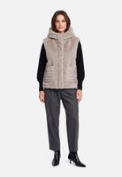 Frau trägt grauen Faux-Fell-Vest, schwarze Bluse und graue Anzughose mit schwarzen Pumps.