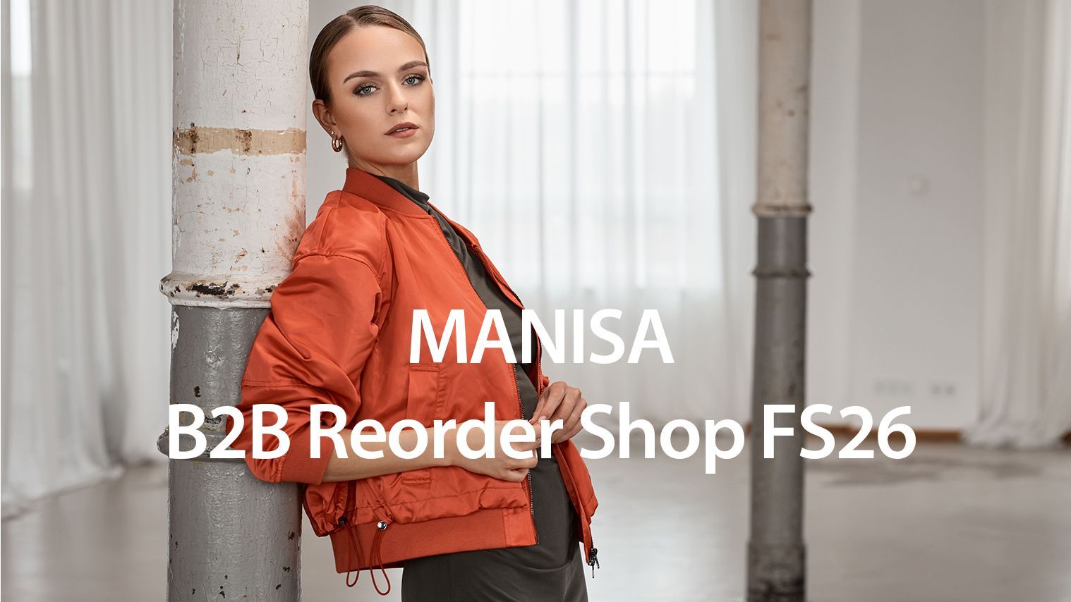 Frau in orangefarbenem Bomberjackett vor grauer Wand, B2B Reorder Shop FS26 von Manisa.