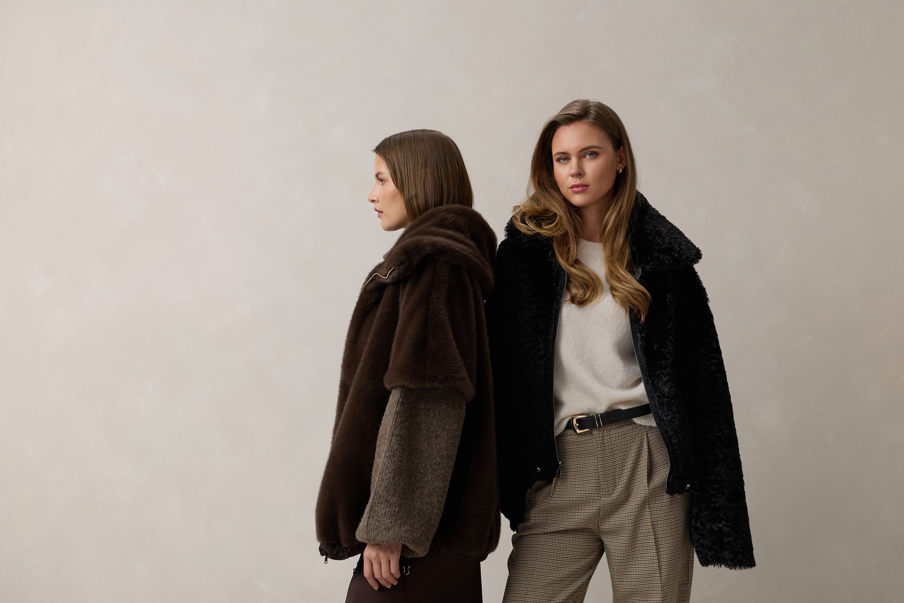 Zwei Personen in stylischen Winteroutfits mit Jacken und unterschiedlichen Hosen, Blick nach vorne.