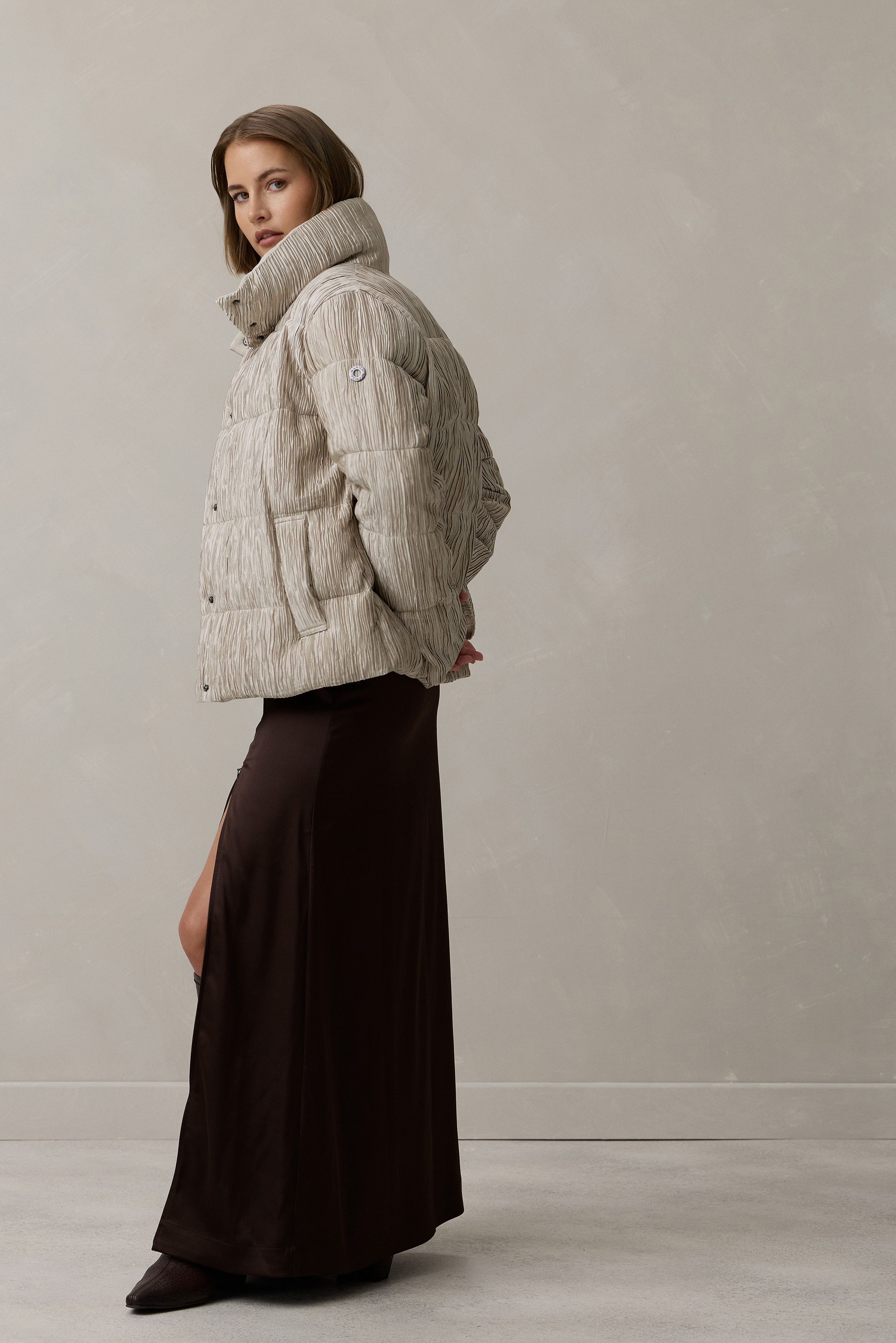 Frau trägt oversized beige Strickjacke mit Skijacke-Stil und langer dunkler Maxirobe, elegant seitlich stehend.