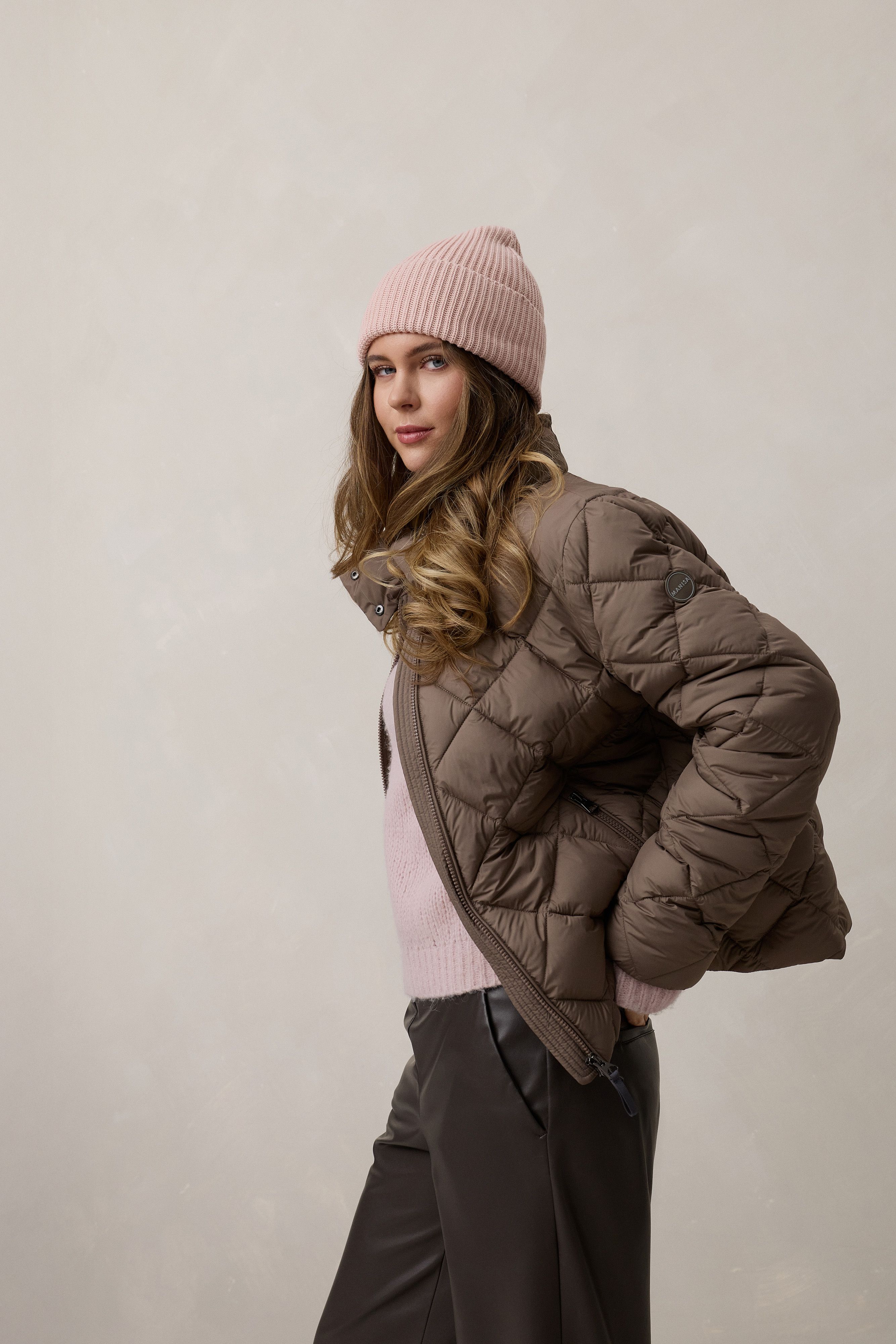 Frau trägt stylischen Pufferjacken-Anzug mit pinkem Schal und Beanie, lässig posierend.