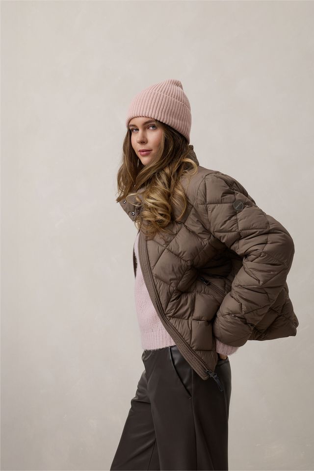 Frau mit pinkem Beanie und braunem Daunenjackett lächelt in winterlicher Kleidung.