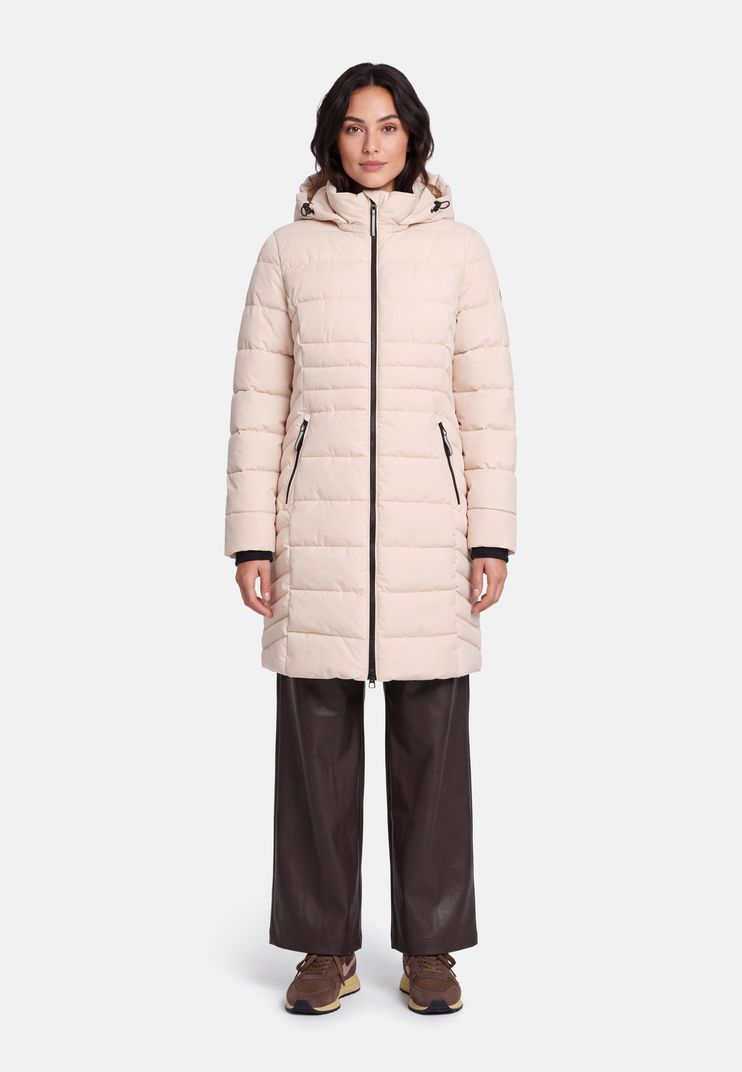 Frau trägt beige Daunenjacke mit Kapuze, dunkle Hosen und braune Sneakers.