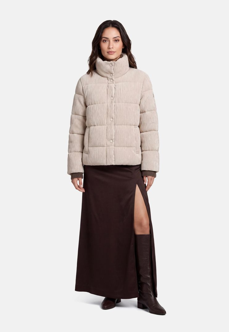 Frau trägt beige Puffermantel mit Knopfleiste, langer dunkler Rock mit Schlitz und schwarze Kniehochstiefel.